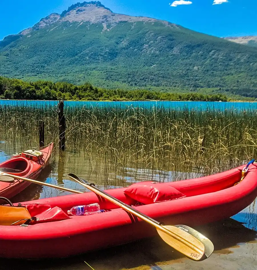 Kayak gonflable rouge et sa pagaie au bord d'un lac, entre les roseaux, montagnes en arrière-plan
